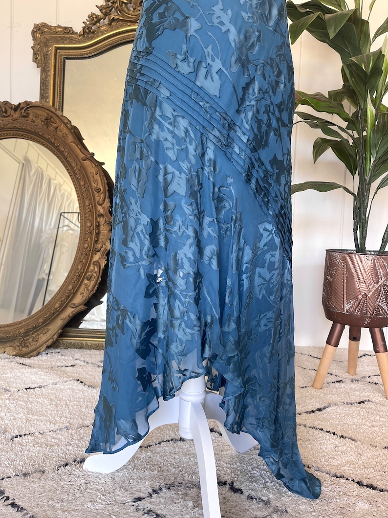 May include: A blue maxi dress with a floral pattern. The dress has a flowing skirt and a fitted bodice. The dress is made of a soft, lightweight fabric.