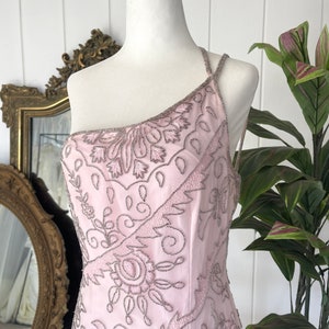 May include: A pink one-shoulder dress with a beaded floral pattern. The dress is made of a sheer fabric and has a fitted silhouette.