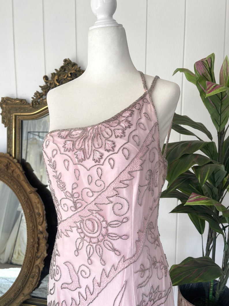 May include: A pink one-shoulder dress with a beaded floral pattern. The dress is made of a sheer fabric and has a fitted silhouette.