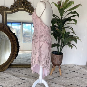 May include: A pink, high-low, beaded dress with a halter neckline and a floral pattern. The dress is on a white mannequin and has a high-low hemline.