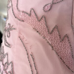 May include: Close-up of a pink fabric with silver bead embroidery. The embroidery forms a floral pattern.