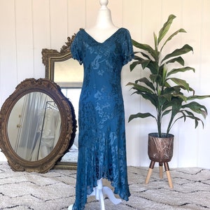 May include: A teal blue silk dress with a floral pattern and a v-neckline. The dress has short sleeves and a high-low hemline.