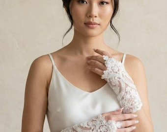 Op de afbeelding: Elegante witte kanten vingerloze handschoenen met bloemen- en krulpatronen. De handschoenen zijn ontworpen met ingewikkelde details, perfect voor bruiloften of speciale gelegenheden. Het delicate kant voegt een vleugje verfijning en romantiek toe.