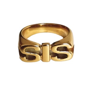 Könnte beinhalten: Goldring mit dem Wort "SIS" in fetten Buchstaben.