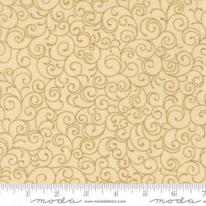 May include: A light beige fabric featuring a repeating pattern of metallic gold swirls and flourishes. A white ruler is visible at the bottom edge, showing measurements in inches, with the text moda and www.modafabrics.com printed on it.
