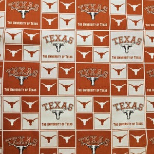 May include: A fabric pattern featuring a repeating grid of burnt orange and white squares. The design includes the text "TEXAS" and "THE UNIVERSITY OF TEXAS" alongside a longhorn steer head logo printed in white or burnt orange ink.