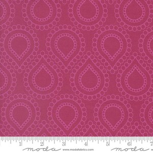 May include: A magenta fabric featuring a repeating pattern of teardrop shapes outlined in small circles. A white ruler is visible at the bottom edge, showing measurements in inches, with the text moda and www.modafabrics.com printed clearly.