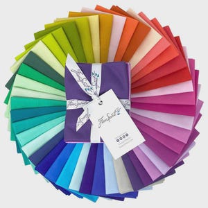 Pode incluir: Um arranjo circular de quadrados de tecido dobrados num espectro de cores incluindo verde, amarelo, laranja, vermelho, rosa, roxo e azul. Uma fita branca com o texto Free Spirit ata a pilha, com uma etiqueta marcada Free Spirit.