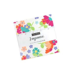 Può includere: Una pila di pezzi di tessuto quadrati con sfondo bianco e un colorato motivo floreale di fiori rosa, arancioni, blu e viola con foglie verdi. Una fascia di carta bianca con l'etichetta Joysome by Corey Yoder of Coriander Quilts avvolge il tutto.