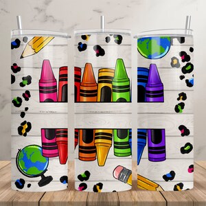 May include: Three stainless steel tumblers with a white woodgrain background. Each tumbler features a different design with a school theme. One tumbler has a pencil, a globe, and crayons. Another tumbler has a pencil and crayons. The third tumbler has a globe and crayons.