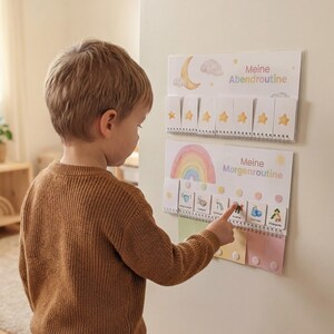 Kleiner Junge steht vor seinem Montessori Routineplaner Regenbogen an der Wand und zeigt selbstständig auf eine Routinekarte der Morgenroutine