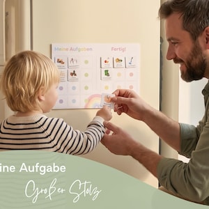 May include: A white magnetic chore chart titled Meine Aufgaben and Fertig with colorful icons and grid spaces. The chart features a rainbow graphic at the bottom and includes small square task cards that can be moved to track daily responsibilities.