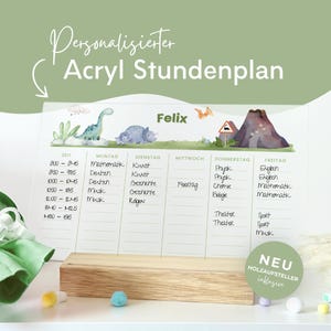 Könnte beinhalten: Ein transparenter Acryl-Stundenplan mit Dinosaurier-Motiven, darunter ein grüner Dinosaurier, ein blauer Triceratops und ein Vulkan. Das Board zeigt den Namen Felix und steht auf einem Holzsockel. Text: "Personalisierter Acryl Stundenplan" und "NEU HOLZAUFSTELLER inklusive".