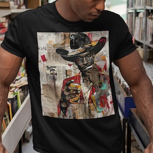 May include: A black t-shirt with a colorful graphic print of a person wearing a cowboy hat, sunglasses, and a red jacket. The person is holding a glass of liquid and smoking a cigarette. The graphic is set against a background of newspaper clippings and abstract shapes.