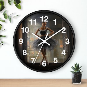 May include: Black round wall clock featuring a ballerina in a black dress. The clock face has white numerals and hands. The ballerina is standing in front of a window. The clock has a black frame and is on a wooden surface.