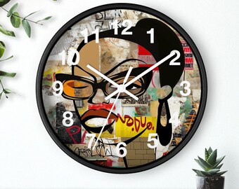 May include: A round wall clock with a black frame. The clock face features a colorful collage of a woman's face with glasses, bold red lips, and the numbers 1 through 12. The clock hands are white.