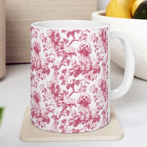 May include: White ceramic mug with a pink floral pattern featuring a repeating design of small dogs. The mug has a large handle.