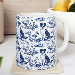 May include: White ceramic mug with a blue and white pattern of border collies sitting in a floral design.