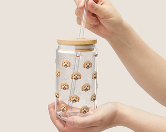 May include: A clear glass jar with a wooden lid and a straw. The jar is filled with a pattern of small dog faces. The jar is being held by a hand.