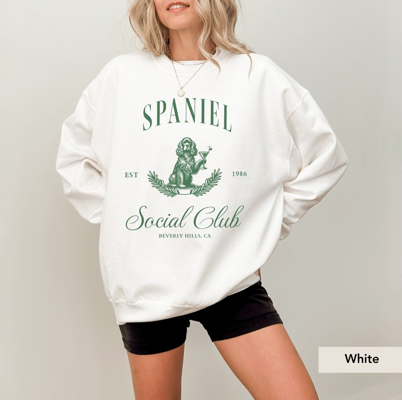 May include: White sweatshirt with a green graphic design of a dog holding a martini glass. The graphic says "Spaniel Social Club Est 1986 Beverly Hills, CA."