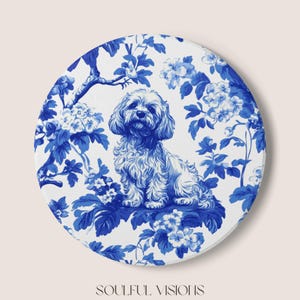 May include: Round, white coaster with a blue and white floral design and a seated dog illustration. The dog is a fluffy breed, and the floral pattern resembles classic porcelain. The text "SOULFUL VISIONS" is at the bottom.