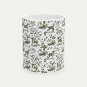 May include: White ceramic mug with a repeating pattern of dogs and foliage in a muted green hue. The design is reminiscent of a traditional toile print, giving a vintage feel. The mug is cylindrical and of a standard size.