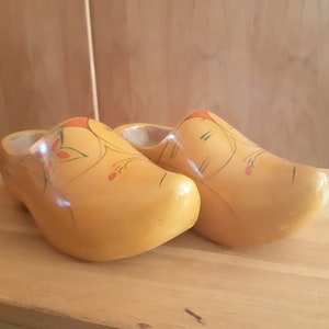 Puede incluir: Un par de zuecos de madera amarillos con diseños florales pintados a mano en rojo, verde y naranja.