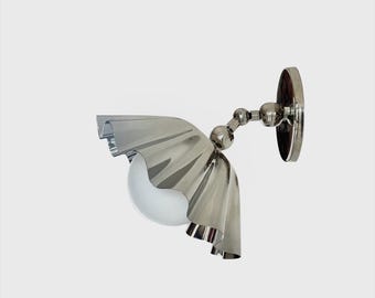 May include: A modern wall sconce with a polished chrome finish. The fixture features a decorative, ruffled shade and a spherical, frosted glass bulb. The sconce is mounted on a round backplate and has an adjustable arm.