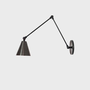 Puede incluir: Una lámpara de pared negra y ajustable con una pantalla cónica. La lámpara tiene un brazo giratorio y una base circular para el montaje. La pantalla es de color gris oscuro y el diseño es minimalista y moderno.