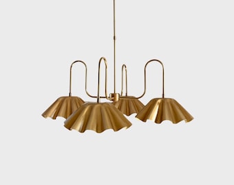 May include: A gold-colored chandelier with four lights. Each light has a ruffled, umbrella-shaped shade. The fixture has a central stem and curved arms extending to each light. The design is modern and elegant.