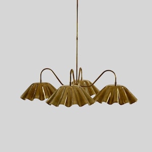 May include: A brass chandelier with five scalloped shades. The light fixture has a central stem and curved arms extending to each shade. The shades have a ruffled edge and a warm, metallic finish. The fixture is suspended from a circular ceiling mount.