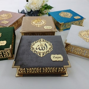 May include: Set of six small decorative boxes with gold trim and a velvet fabric exterior. Each box features a gold Arabic calligraphy design and a personalized name tag. The names on the boxes are: Zayin, Ayal, Haris,  Leyan,  Mizan, and a name that is not visible in the image.