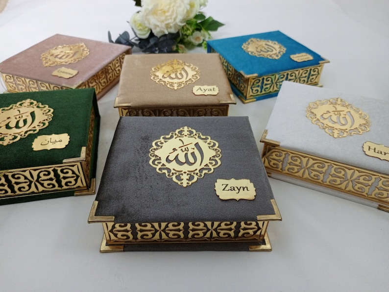 May include: Set of six small decorative boxes with gold trim and a velvet fabric exterior. Each box features a gold Arabic calligraphy design and a personalized name tag. The names on the boxes are: Zayin, Ayal, Haris,  Leyan,  Mizan, and a name that is not visible in the image.