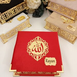 May include: Three decorative boxes with gold trim and intricate designs. The boxes are covered in velvet fabric in black, pink, and red. The boxes have a gold inscription of the Arabic word for God, "Allah", and a gold label with the text "Ramadan Mubarak", "Ramadan Kareem", and "Rayan".