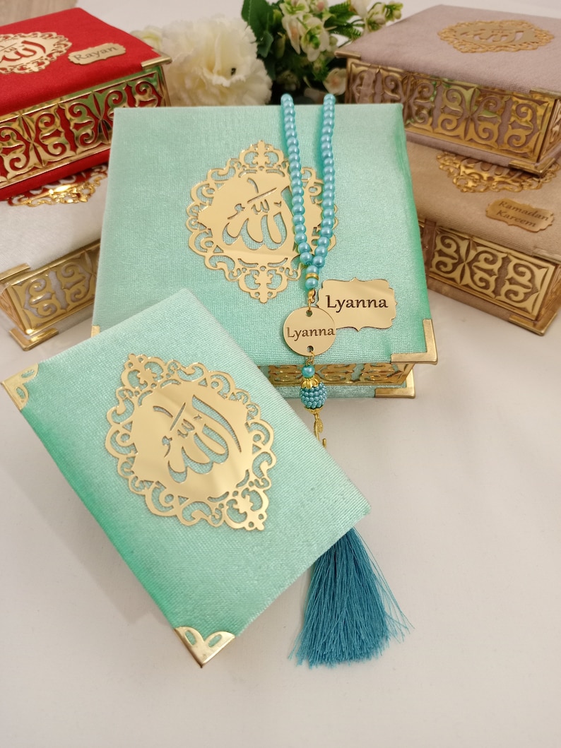 May include: A set of three decorative boxes with gold trim and a green box with a gold inscription of the word "Allah" in Arabic. The boxes are covered in a soft, velvety fabric. A blue tassel hangs from the green box. A blue beaded necklace with a gold pendant that reads "Lyanna" is included.