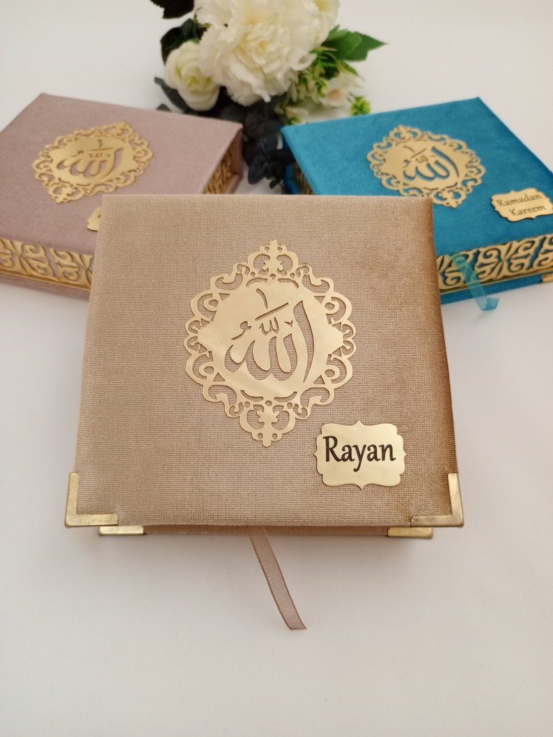 May include: Three decorative boxes with gold Arabic calligraphy and a gold inscription that reads "Rayan". The boxes are covered in fabric and have gold accents. The boxes are on a white surface.