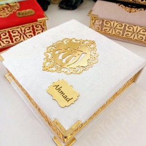 May include: A white velvet box with gold trim and a gold Arabic calligraphy design. The box has a gold nameplate that says "Ahmad".