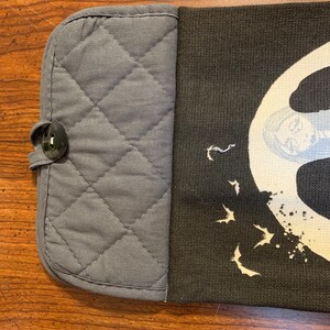 May include: A gray quilted oven mitt with a black button and a black fabric panel with a white design of bats and a moon. The design also includes a white splatter pattern.