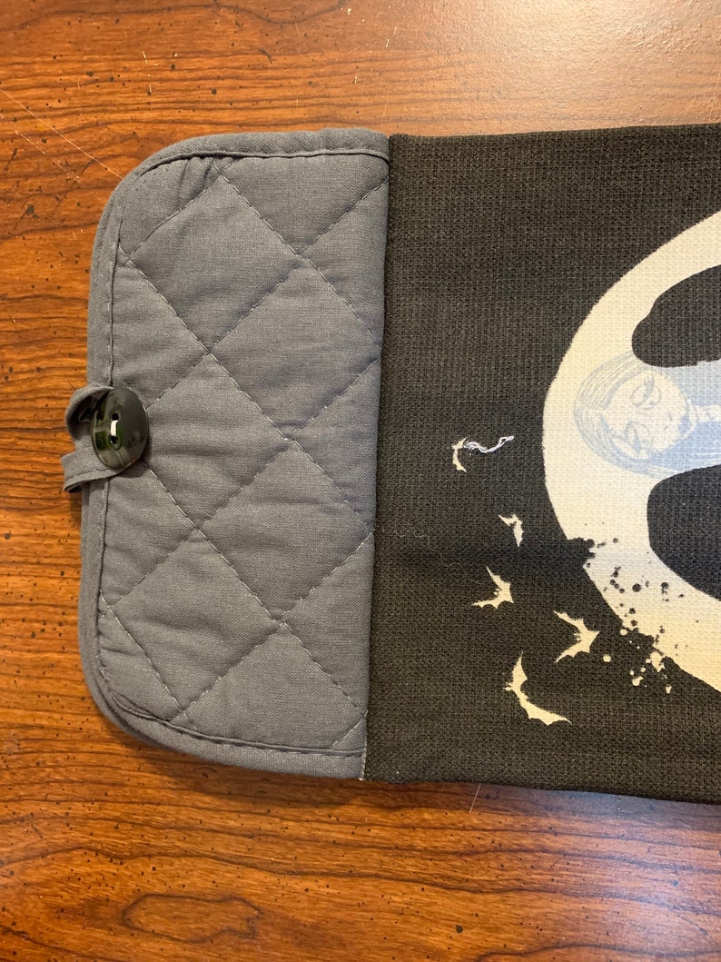 May include: A gray quilted oven mitt with a black button and a black fabric panel with a white design of bats and a moon. The design also includes a white splatter pattern.