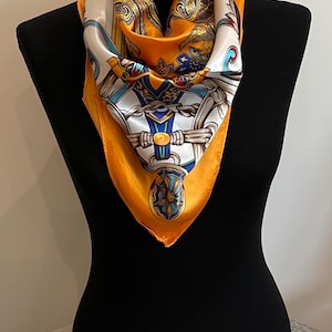 May include: A yellow silk scarf with a white, blue, and gold paisley pattern. The scarf is folded into a triangle shape and is displayed on a black mannequin.