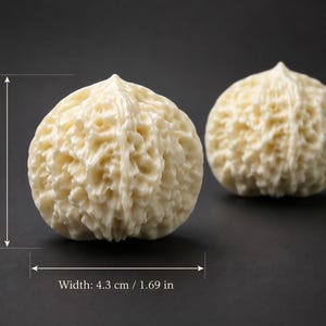 May include: Two off-white, walnut-shaped objects with a textured surface, each measuring 1.69 inches in height and width. The objects are set against a dark background, showcasing their detailed, organic forms.