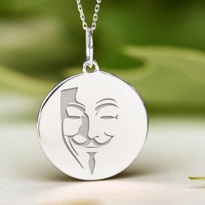 May include: A silver necklace with a round pendant featuring a stylized image of the Guy Fawkes mask.