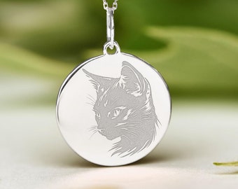 May include: A silver necklace with a round pendant featuring an engraved image of a cat's face.