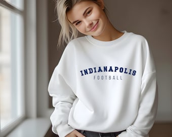 Könnte beinhalten: Weißer Pullover mit einem dunkelblauen Bogen-Design, auf dem "Indianapolis Football" steht.