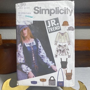 May include: A vintage Simplicity sewing pattern featuring a woman in a medieval-inspired outfit. The pattern includes designs for tops, a corset, a hat, and a bag. The text "JR. TREND" is prominently displayed.