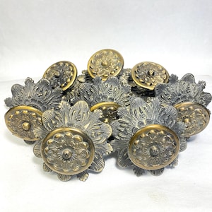 May include: A collection of antique brass floral drawer pulls. Each pull features a round, embossed center with a detailed floral design, surrounded by ornate, stylized leaves. The pulls have a vintage, aged appearance.