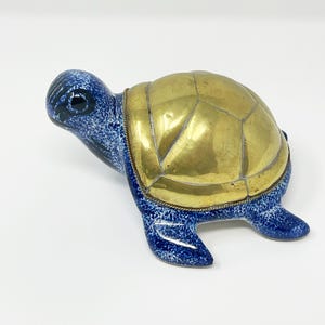 May include: A ceramic turtle ornament with a blue speckled body and a gold-coloured metal shell. The turtle's head and feet are blue, and the shell is segmented. The figurine is a decorative item.