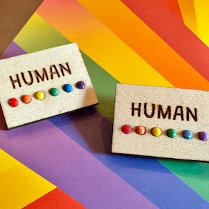 Puede incluir: Dos letreros de madera con la palabra "HUMAN" impresa en ellos. Cada letrero tiene una fila de puntos coloridos del arcoíris.