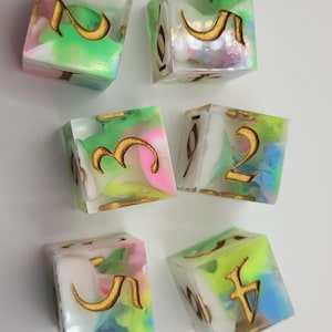 May include: Six handmade dice with colorful swirls of pink, green, and blue. The dice are clear with gold-colored numbers. The dice are a unique set for tabletop games.