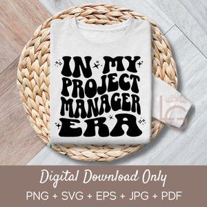 May include: White long-sleeve shirt with the text "IN MY PROJECT MANAGER ERA" in black, retro-style font. The shirt is displayed on a woven, circular placemat. The words "Digital Download Only" are at the bottom.